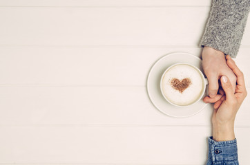 Couple in love holding hands with coffee on white wooden table. Photograph taken from above, top...