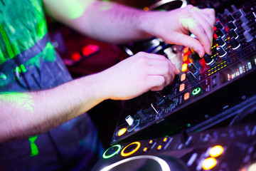 DJ playing music at mixer closeup and mixes the track in the nightclub at party