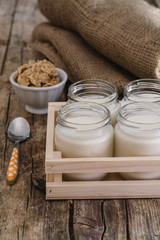 Homemade yogurt in glass jar and wooden box. Antique wooden table. Burlap and cereal bowl on background. Steel teaspoon orange and white dots