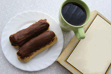 Chocolate eclairs, cup of coffee and book