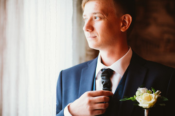 portrait of a young groom standing near window