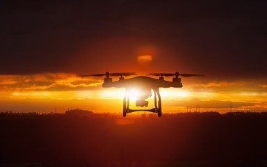 Silhouette of flying drone in glowing red sunset sky