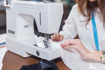 Cropped image of female tailor stitching fine lace with sewing machine sitting in dressmaking studio - obrazy, fototapety, plakaty