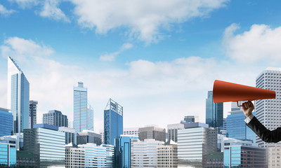 Hand of businesswoman holding red paper trumpet against cityscape background