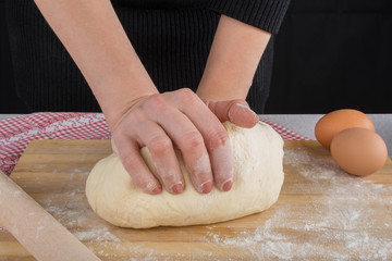 Hardworking female hands kneading dough on wooden kitchen table