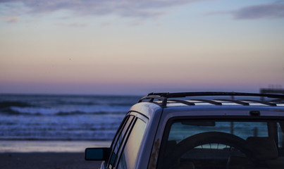Car sitting on the beach with a sunset over the water