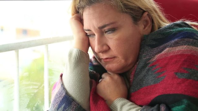 Unhappy, lonely  woman looking the rain falling through a window at home