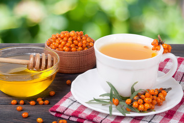 Tea of sea-buckthorn berries with honey on wooden table blurred garden background