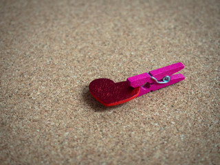 Pink wooden clip with red heart on cork board.