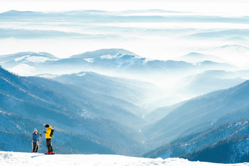Male and female skiers getting ready to slide down the hill from the top of a mountain