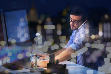 Young man working at office and night cityscape reflection on window