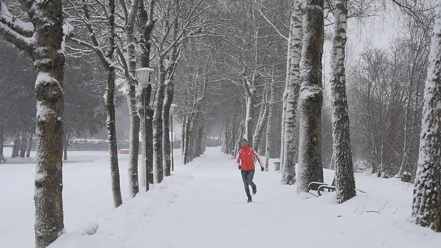 Slow motion of joyful girl running and jumping in winter park enjoying snowfall