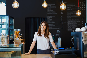 Young female barista standing behind the bar in cafe smiling - obrazy, fototapety, plakaty