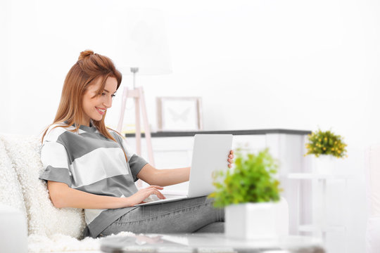 Young beautiful woman using laptop on sofa at home
