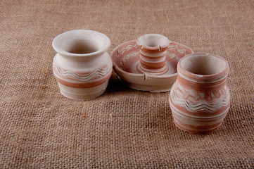 Pottery. Jugs and candlestick made of clay on sackcloth background