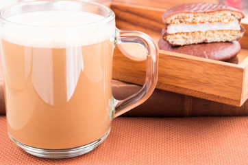 Glass mug with hot cocoa and chocolate biscuits in a wooden tray