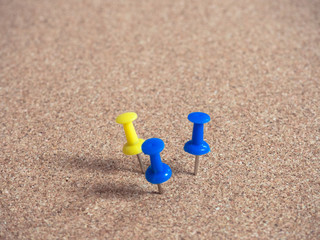 Fototapeta na wymiar Blue and yellow pins on brown cork board.