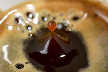 macro drop of coffee in fall toward the cup of coffee