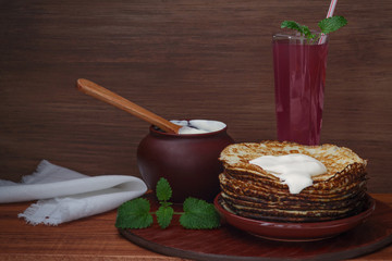Pancakes, sour cream and pudding - dishes of European cuisine. Traditional Slavic food. On a brown background, the pot, tumbler, plate, spoon, napkin. A stack of pancakes. A rustic style.
