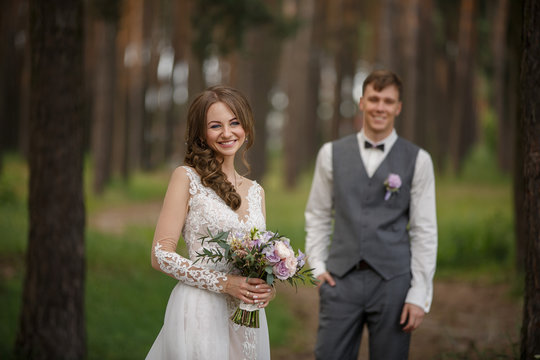 Wedding photo, beautiful bride holding bouquet of fresh flowers and looks to camera on elegant groom background