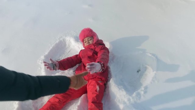 Child in the snow.Young, pretty mother playing on snow-covered yard with a child(girl) Child portrays an angel in the snow