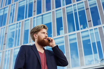 Handsome bearded hipster with serious emotion on red brick wall background. High detailed close up portrait of european 25 years man in summer time.