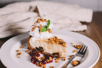 Cheesecake, served with a scoop of ice cream, mint and cranberry jam on a round white plate with crumpled old gray dishcloth in the background