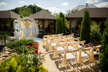 Wedding place setting, chairs with golden decor and wedding arch with fresh flowers