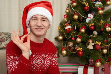 Young man in christmas decoration. Home interior with gifts and fir tree. New year holiday concept.