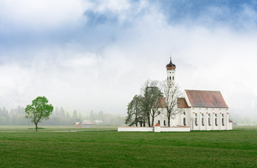 St. Coloman / Schwangau church nearby Neuschwanstein castle in Bavaria region, Germany. Spring misty scene. Green grass meadow at landscape foreground. Place of catholic worship.