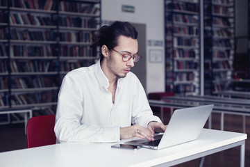 Fototapeta premium Businessman, university student writing and working at laptop, in a public co-working or library