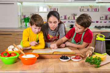 Three kids reading the cook book, making the dinner