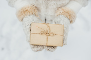 Valentines concept. Female hand in a white knitted mittens holding present gift box on winter background for St. Valentines day.