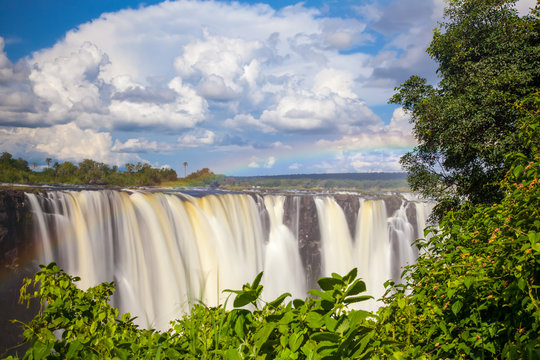 Victoria Falls.  Frontal view with a rainbow.  Taken with an MD filter.  Blue sky with clouds looming.