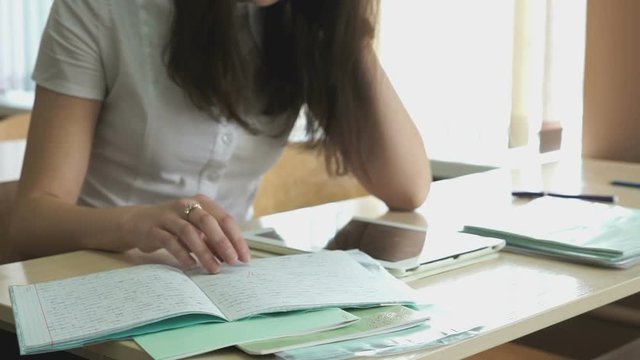 The girl sitting at the desk reads the text using the silver computer tablet