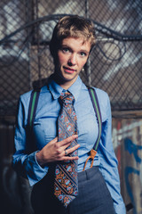 Young androgynous woman dressed in mens clothing in a grungy, urban outdoor location