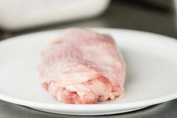 Raw chicken meat with skin, single piece of deboned chicken leg on a white plate