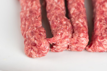 Raw kebabs on a white plate, shot close up, minced meat special before grilling