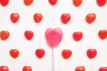 Pink Valentine's day heart shape lollipop with small red candy in cute pattern on empty white paper background. Love Concept. colorful hipster style. Knolling top view.