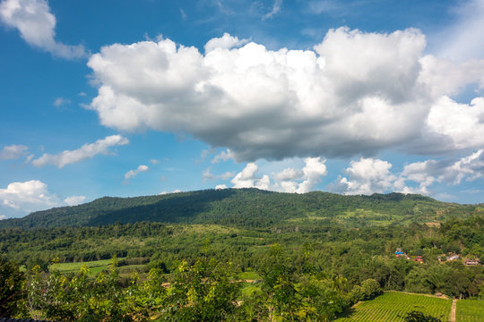 Mountain by green grass and cloudy blue sky