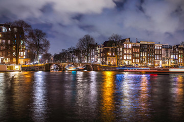 Fototapeta premium AMSTERDAM, NETHERLANDS - JANUARY 12, 2017: Beautiful night city canals of Amsterdam with moving passanger boat. January 12, 2017 in Amsterdam - Netherland.