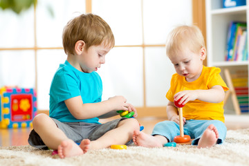 Children play with educational toys in preschool or kindergarten. Toddler kid and baby build pyramid toys at home or daycare.