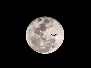 Silhouette of an airplane flying across a full moon.