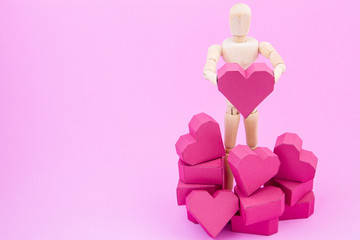 Wooden dummy holding paper box red heart shape on pink backgroun