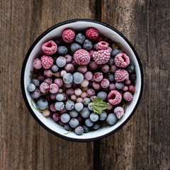 frozen berries, black currant, red currant, raspberry, blueberry in enamelled bowl decorated by currant leaf on wooden table in rustic style,  top view. - 133474016
