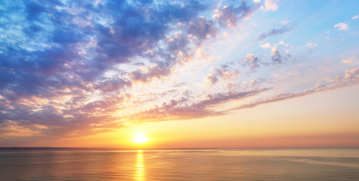 Panorama view of sunset sunrise sea ocean summer with textured clouds and beautiful sunlight in blue gold tones. Romantic tender wallpaper, soft air harmonious stunning artistic image.