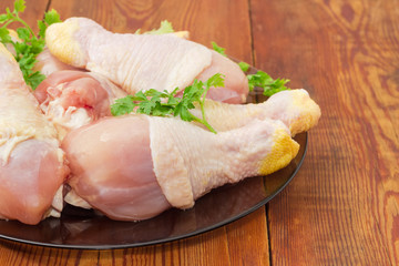 Uncooked chicken legs with greens on glass dish closeup