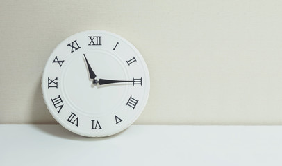 Closeup white clock for decorate show a quarter past eleven or 11:15 a.m. on white wood desk and cream wallpaper textured background with copy space