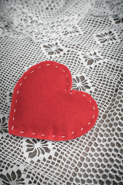 Valentine's card. Red felt heart on lace and wooden vintage table. Soft focus.