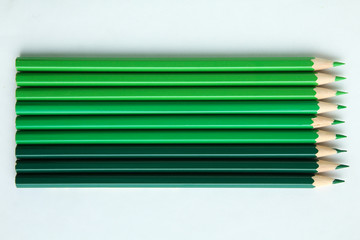 Green pencils of different colors lying on a white background.